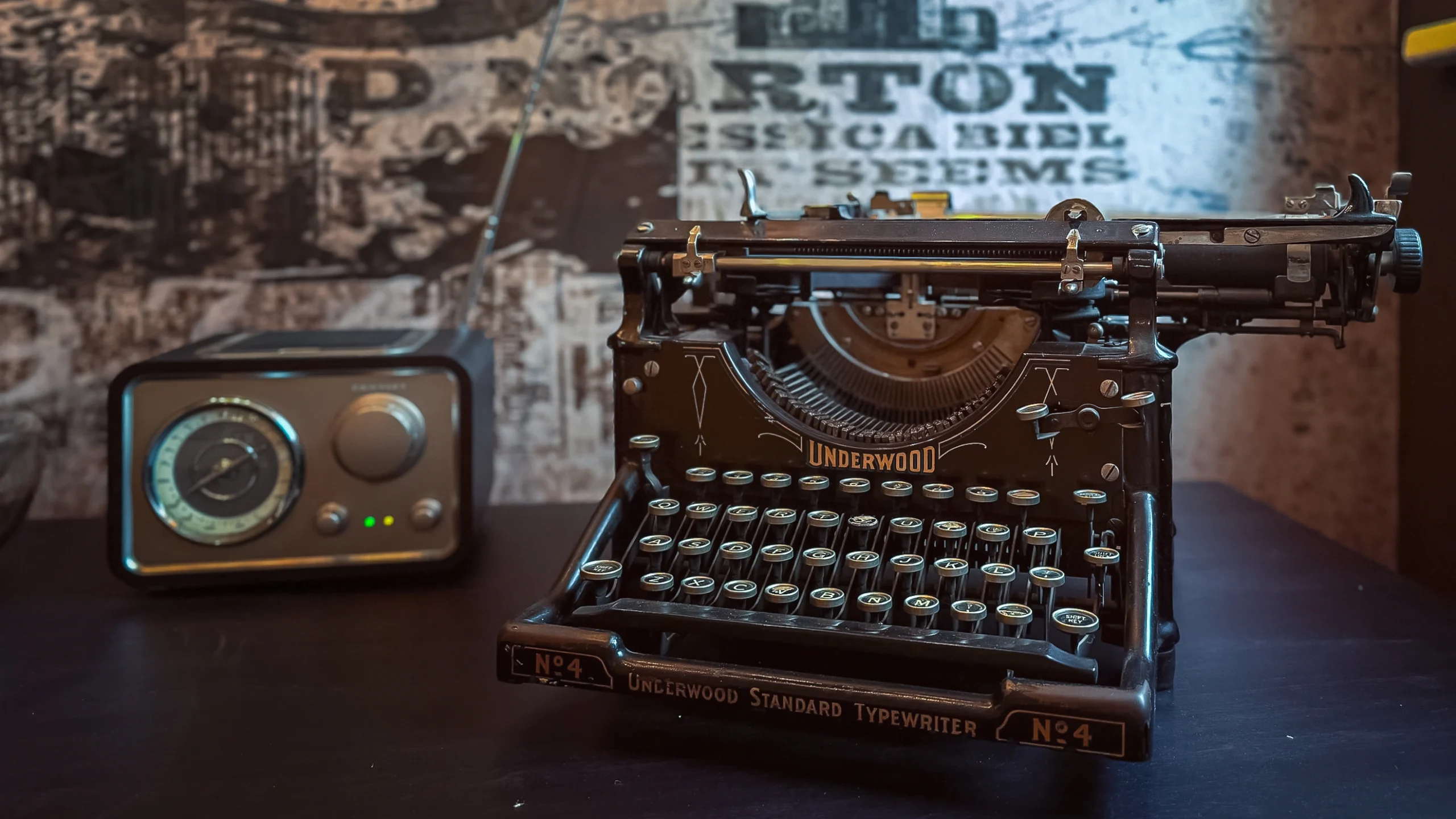 Close-up of a vintage black Underwood Standard Typewriter No. 4 next to a retro silver and black radio, set against a blurred, graphic mural wall.